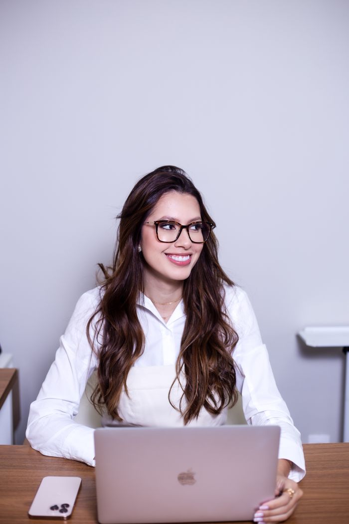 Mastering the First Impression: Your intriguing post title goes here Smiling woman in glasses using a laptop at a desk, displaying a professional work environment.