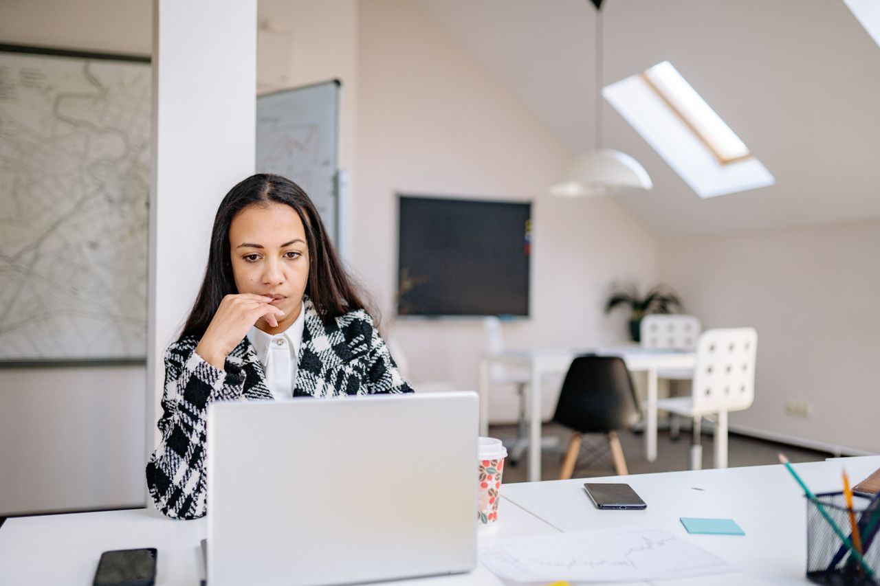 Woman in stylish office working on laptop with natural lighting.